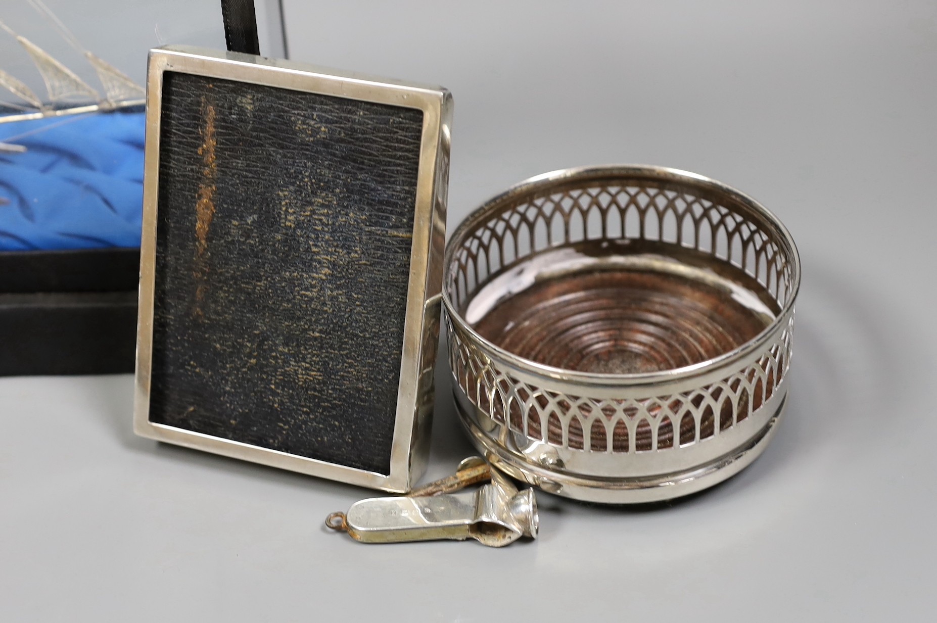 A group of silver and white metal items including a cased boat model, cigar cutter and mounted photograph frame and plated items